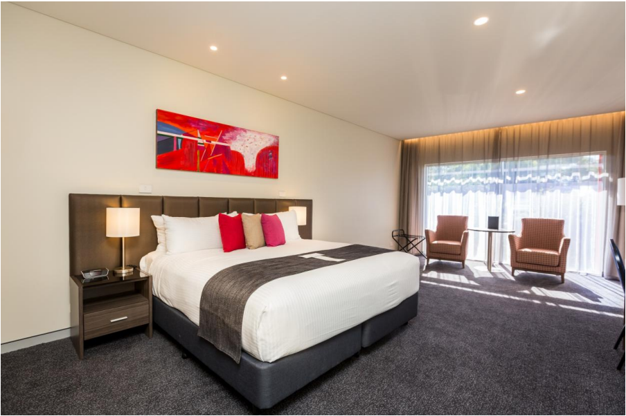 Redlands Rugby Union Club Modern hotel room with a large bed, bedside tables, lamps, two armchairs by a window, and a red abstract painting above the bed.