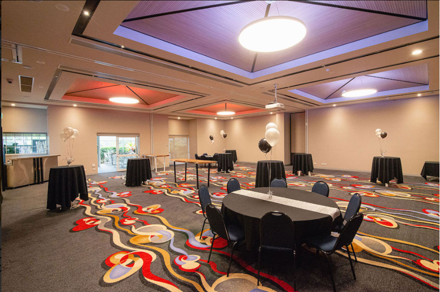 Redlands Rugby Union Club Spacious event room with round tables and black tablecloths, balloon decorations, modern lighting, and colorful patterned carpet.