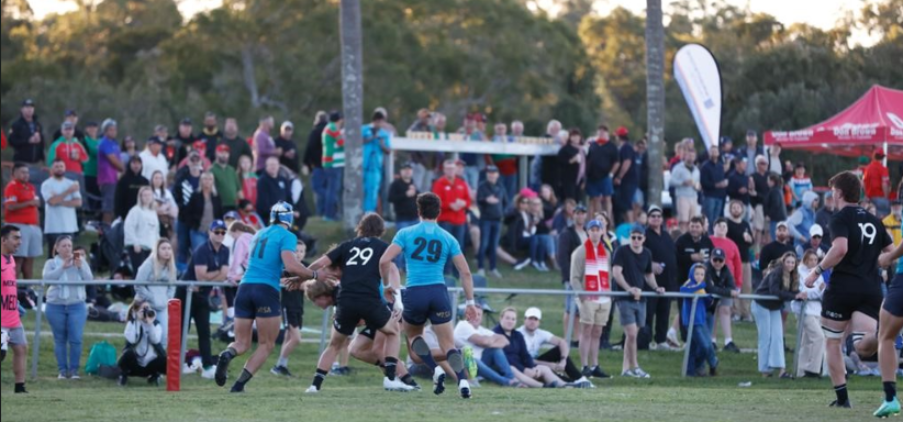 Redlands Rugby Union Club Rugby players in blue and black jerseys compete on a grassy field as a large crowd watches from the sidelines.